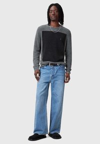 Grijs en zwarte trui met een blokontwerp, gecombineerd met lichtblauwe wijde jeans en zwarte instap schoenen. Eenvoudige zilveren ketting.