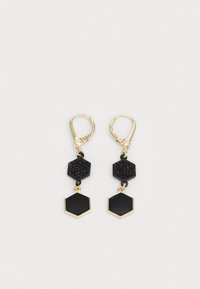 Orecchini in tono oro con due forme esagonali nere; una ha una superficie testurizzata, l'altra ha una finitura liscia, entrambe pendono da un gancio leverback.