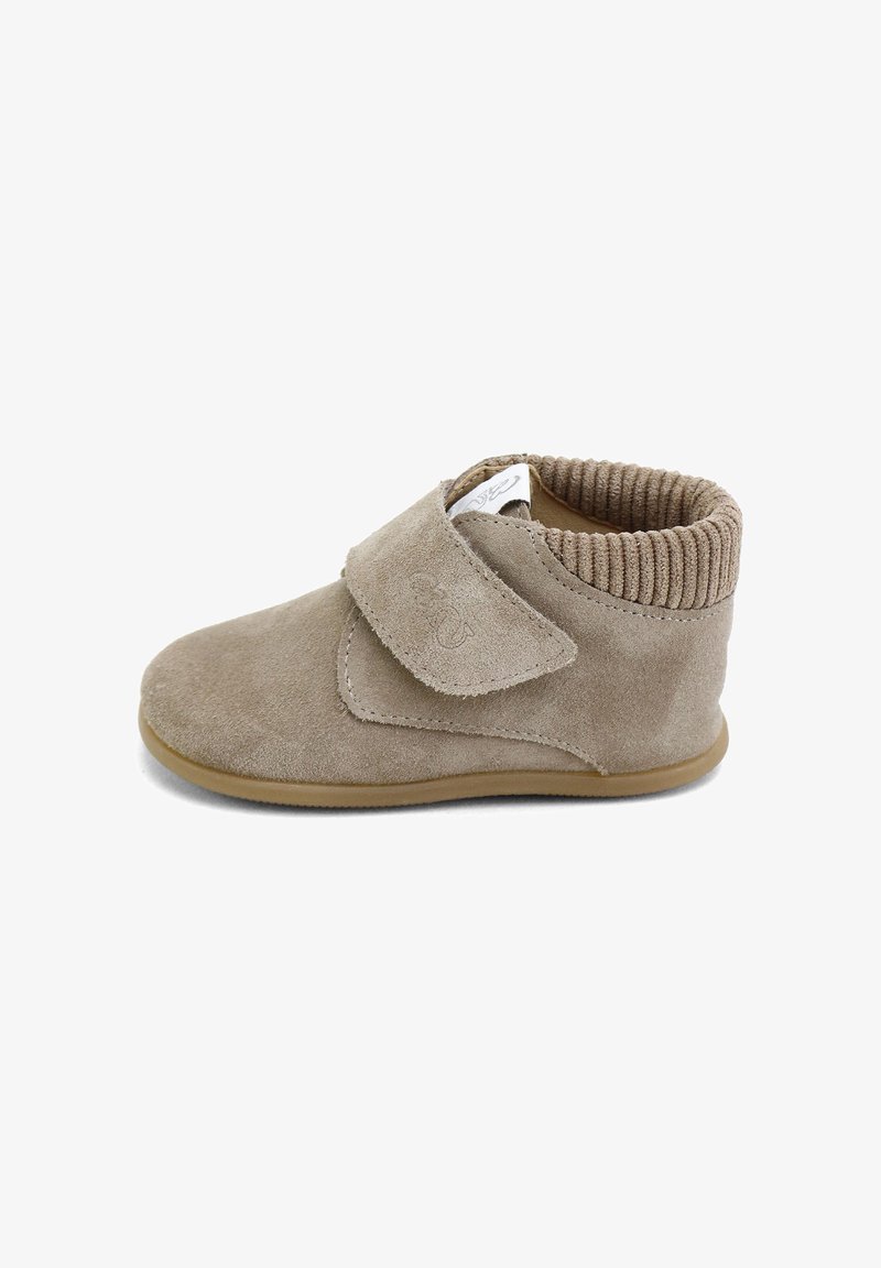 Botín de ante beige con un collar tipo calcetín ribeteado, correa de Velcro ajustable y suela de goma para tracción. Textura suave y diseño minimalista.