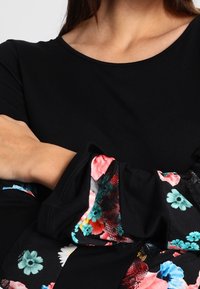 Svart långärmad tröja med ett blommönstrat tyg vid mudden i livfulla färger, med en slät textur och rund halsdesign.