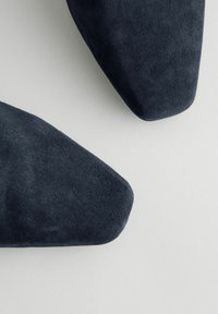 Chaussures en suede gris foncé avec un design à bout pointu. La texture est douce et la forme est épurée, sans accents ni motifs visibles.