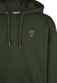 Dark green hoodie made of soft, textured fabric. Features a pink embroidered bird logo, silver hardware, and a front pocket.