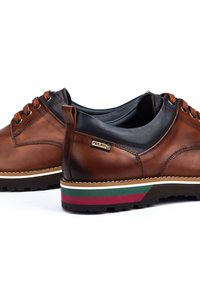 Des chaussures en cuir marron avec un dessus en cuir noir, une semelle à rayures multicolores et des lacets orange. Présente un logo de marque sur le côté.