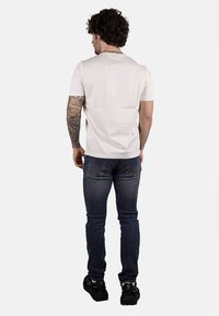 T-shirt bianco in cotone con maniche corte, abbinato a jeans in denim blu. La t-shirt ha un design minimalista; i jeans presentano tasche posteriori.