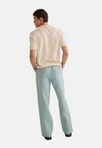 Polo en tricot beige et pantalon en lin bleu clair. Le polo a des manches courtes et une finition texturée; le pantalon est ample.