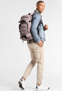Zaino in tessuto rosa testurizzato, con hardware nero, spallacci regolabili, sistema esterno di corda elastica e numerosi scomparti.
