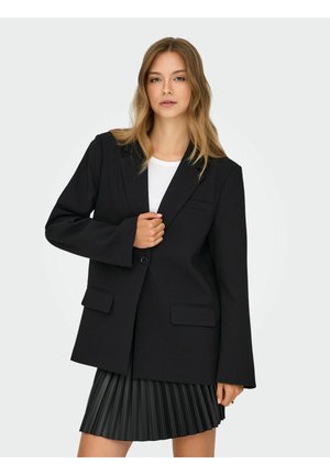 Črn blazer z prilagojeno zasnovo, z vdelanimi ovratniki, z enim gumbom, sprednjimi žepi, oblečen preko bele majice in plisirane krila.