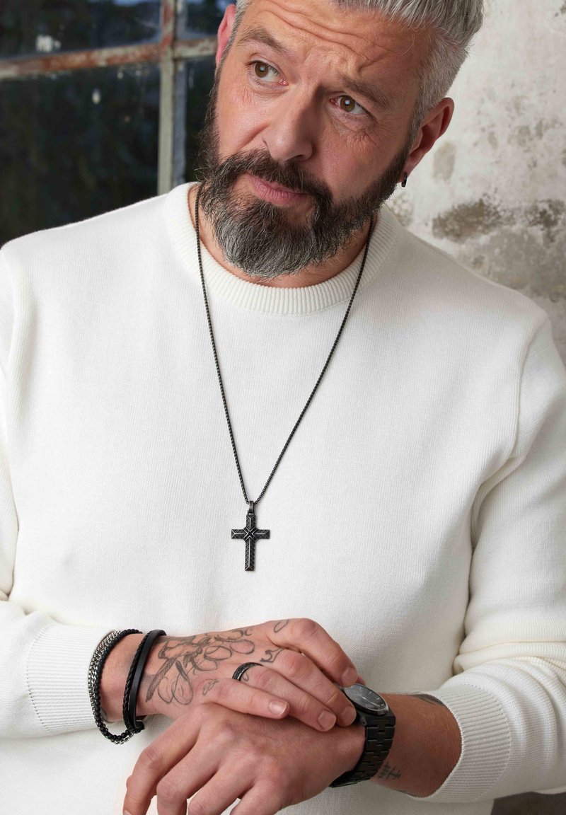 Pull en tricot blanc à col rond, collier en chaîne argentée avec un pendentif croix noir, bracelets en cuir et en métal, et une montre.