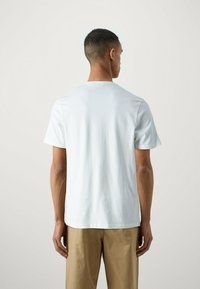 T-shirt bianca a maniche corte in tessuto morbido, con scollatura a girocollo e vestibilità rilassata, abbinata a pantaloni beige. Design minimalista, senza decorazioni.