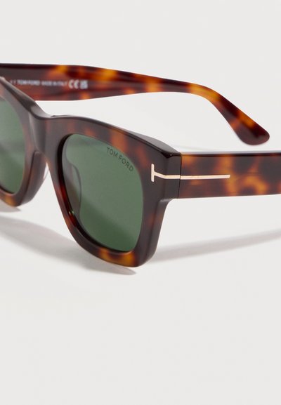 Τετράγωνα γυαλιά ηλίου με μοτίβο χελώνας, πράσινους φακούς και χρυσό λογότυπο σε σχήμα Τ στους βραχίονες.