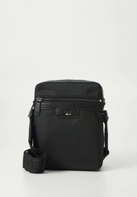 Svart skulderveske i strukturert stoff, med glidelåslukking på toppen, justerbar stropp og en liten logodetalj foran.