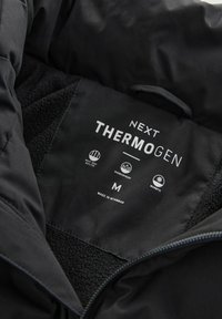 Czarna, izolowana kurtka ma wnętrze z miękką, teksturowaną podszewką. Metka zawiera markę "Thermogen", rozmiar "M" oraz ikony oznaczające uszczelnienie na ciepło, wodoodporność i ciepło.