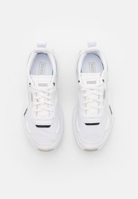 Vita atletiska sneakers med mesh-paneler, platta snören, vadderad krage och grepp-sula; har PUMA-logotyp på tungan och sidodetaljer.