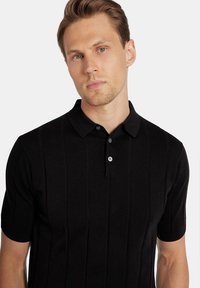 Czarna koszulka polo z krótkim rękawem o teksturowanym, żebrowanym wzorze, z klasycznym kołnierzem i zapięciem na dwa guziki w kontrastującym kolorze.