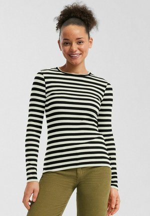 Top de manga larga a rayas blancas y negras, con textura acanalada y cuello redondo. Se lleva con pantalones de pana verde oliva, que muestran una silueta ajustada.