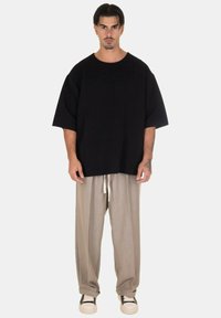 T-shirt nera ampia e testurizzata con maniche larghe, abbinata a pantaloni beige chiaro a pieghe, dotati di vita con cordoncino e sneakers bianche.