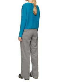 Tiefgrüner gerippter Pullover mit langen Ärmeln, kombiniert mit hoch taillierten, hellgrauen, weit geschnittenen Hose und grünen Schuhen. Schlichtes Design, ohne Muster.