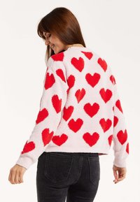 Fluffy, lightweight sweater with a pink base and bold red heart patterns throughout. Features long sleeves and a cropped hem design.