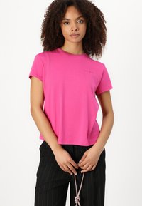 T-shirt in cotone a maniche corte di un vivace colore rosa. Presenta un collo a giro e un sottile logo sul petto. Vestibilità comoda.