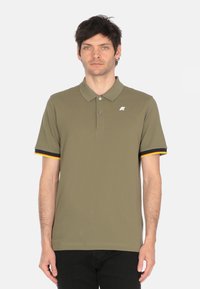 Polo shirt verde oliva realizzato in tessuto liscio, con colletto, tre bottoni e accenti neri e gialli a contrasto sulle maniche.