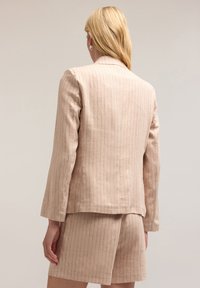 Blazer su misura rosa chiaro con motivo a righe sottili, maniche lunghe e taglio dritto, abbinato a un pantalone corto coordinato.