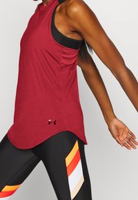 Rode atletische tanktop met een gaas zijzak, afgeronde zoom en logo. Gecombineerd met zwarte leggings met horizontale kleurstrepen.