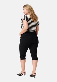 Zwarte gekorte broek met zijsplitten, gecombineerd met een zwart-wit gestreept gebreid bovenstuk met korte mouwen en een ronde hals.