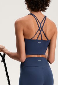 Tengerészi sportmelltartó, keresztezett hátrész pántokkal, elasztikus anyagból készült. Felső része cropped fazonú, és magas derekú leggingshez párosítva.