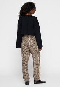 Sort cropped sweatshirt parret med brune slangeprintbukser med glat tekstur og elastiske manchetter, samt sorte slips-on sko.