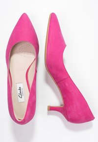 Escarpins en daim rose avec une pointe pointue et un petit talon bloc, dotés d'une doublure douce et d'ouvertures latérales pour un design moderne.