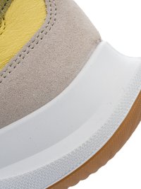 Close-up of a sneaker's heel showing beige suede, yellow leather upper, white midsole, and textured brown rubber outsole.