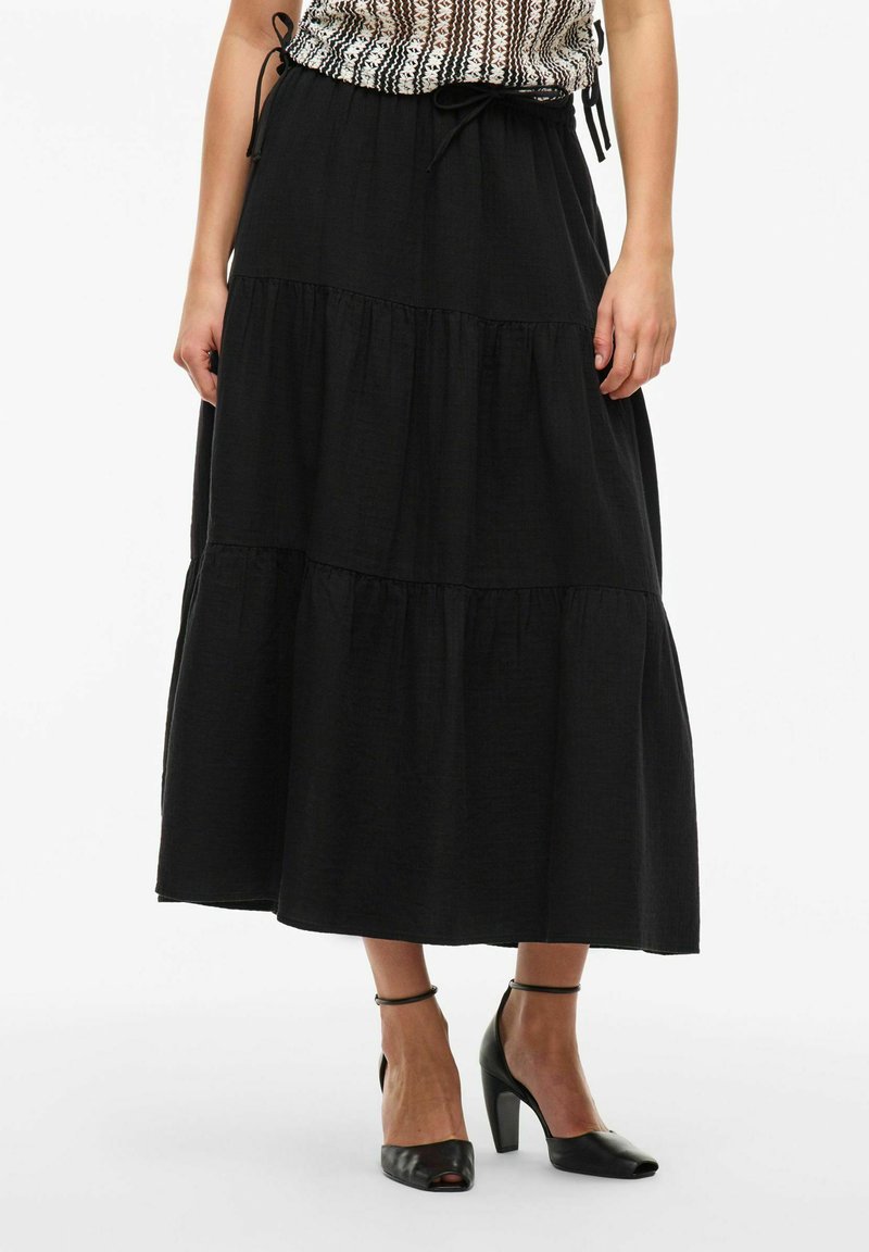 Juodas sluoksniuotas maksi sijonas, pagamintas iš lengvos medžiagos, su elastingu juosmeniu ir raišteliu. Pora su juodais aukštakulniais batais.