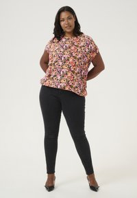 Haut à manches courtes floral avec des motifs roses, violets et jaunes sur fond noir, associé à un jean skinny noir et des escarpins noirs pointus.
