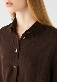 Brown button-up shirt featuring a textured fabric, classic collar, and three gold-tone buttons along the placket.