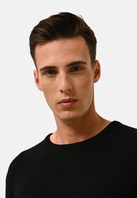 Zwarte ronde hals trui met een zachte textuur, aansluitend ontwerp en ribbelaccenten langs de halslijn en zoom, gedragen door een model met een neutrale uitdrukking.