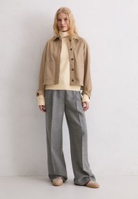 Beżowa krótka kurtka z bocznymi kieszeniami, zestawiona z kremowym prążkowanym golfem i szarymi szerokimi spodniami. Miękkie, casualowe materiały z bawełny.