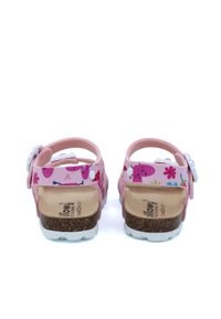 Sandales roses avec une semelle en liège, présentant une sangle à motifs avec des fleurs et des personnages, des accents blancs et des boucles réglables à l'arrière.