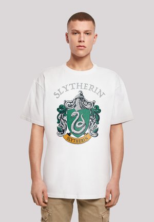 T-shirt en coton blanc avec le blason de la maison Slytherin en vert et noir, accompagné d'un design de serpent et du texte "Slytherin" en gris. Coupe décontractée.