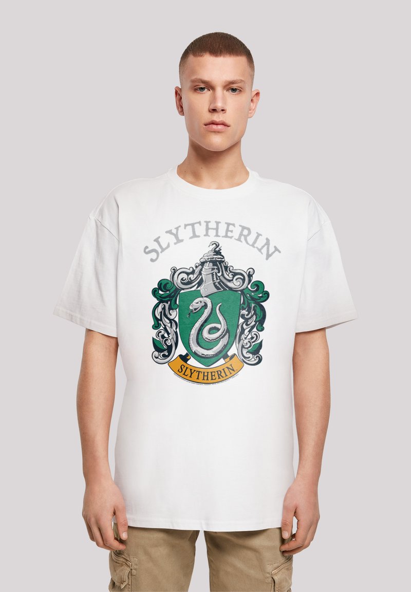 Hvit bomulls t-skjorte med Slytherin husmerke i grønn og svart, med slange-design og teksten "Slytherin" i grått. Avslappet passform.
