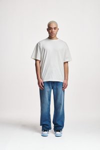Lys grå oversized t-skjorte med korte ermer, sammen med falmede blå jeans. Fottøyet har en hvit base med blå aksenter.