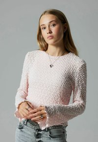 Rosa bluse med lange ærmer og tekstureret blomsterprint, flæsekant ved ærmerne, kombineret med lyse denim-jeans. Synligt sølvsmykke og ringe.