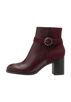 Burgunderfarbene Leder-Ankle-Boots mit glatter Oberfläche, runder Zehenpartie und einem dekorativen Riemen mit einer silbernen Schnalle. Massiver schwarzer Absatz.