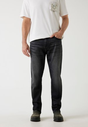 Ciemnoszare dżinsy o prostym kroju, w talii średniego wzrostu, z subtelnymi przejaśnieniami, połączone z białą koszulką z grafiką i ciemnym obuwiem.