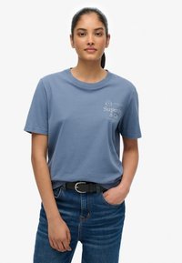 Lyseblå bomulds-t-shirt med korte ærmer, rund hals og hvidt grafisk print foran. Kombineret med højtaljede blå jeans og et sort bælte.