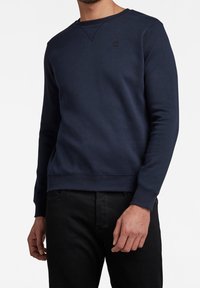 Marineblauer Pullover aus Baumwollmischung mit rundem Ausschnitt, langen Ärmeln, gerippten Bündchen und kleinem Logo auf der Brust.