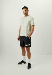 Tricou din bumbac gri deschis, pantaloni scurți negri cu logo-ul alb "NIKE", șosete albe și adidași negri. Design simplu, croială lejeră.
