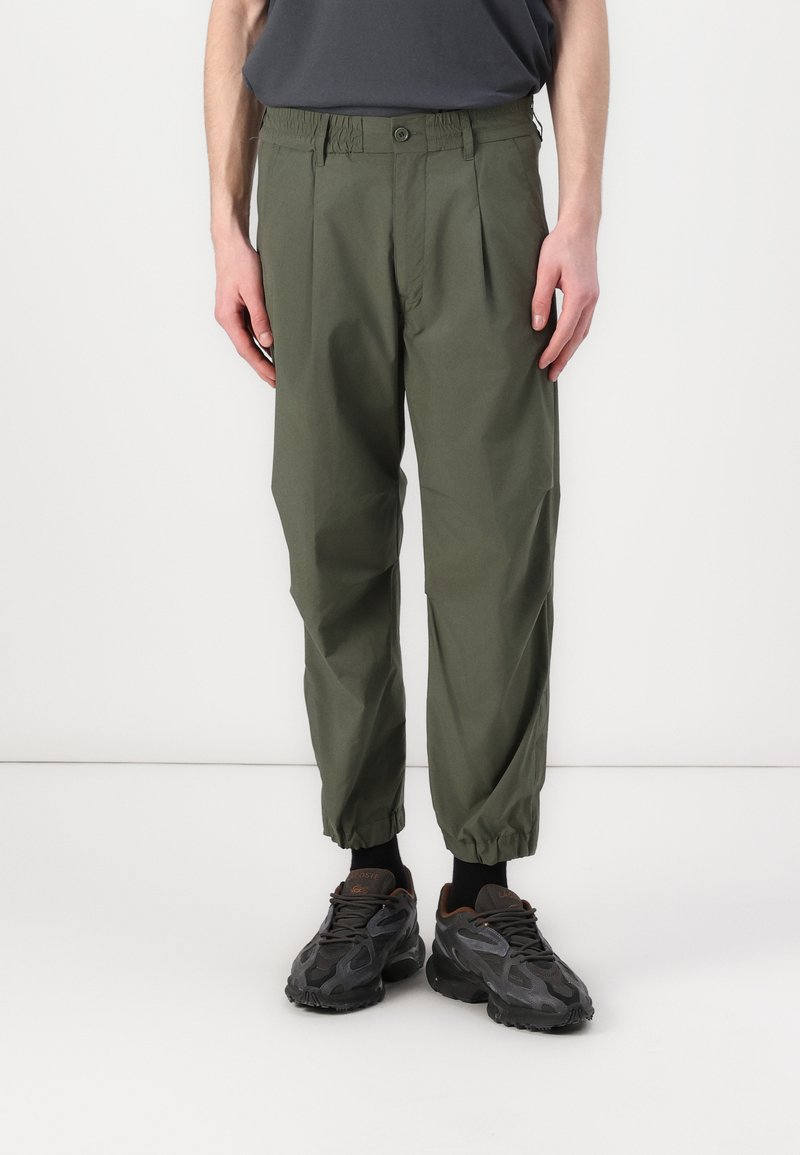 Pantalons plissés verts avec une taille élastique et des poignets ajustés. Fabriqués en tissu léger, avec des poches latérales et une fermeture à bouton.