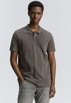 Donkergrijze polo met korte mouwen en een kraag, voorzien van een enkele knoopsluiting en subtiele stiksels. Gecombineerd met lichtgrijze spijkerbroek.
