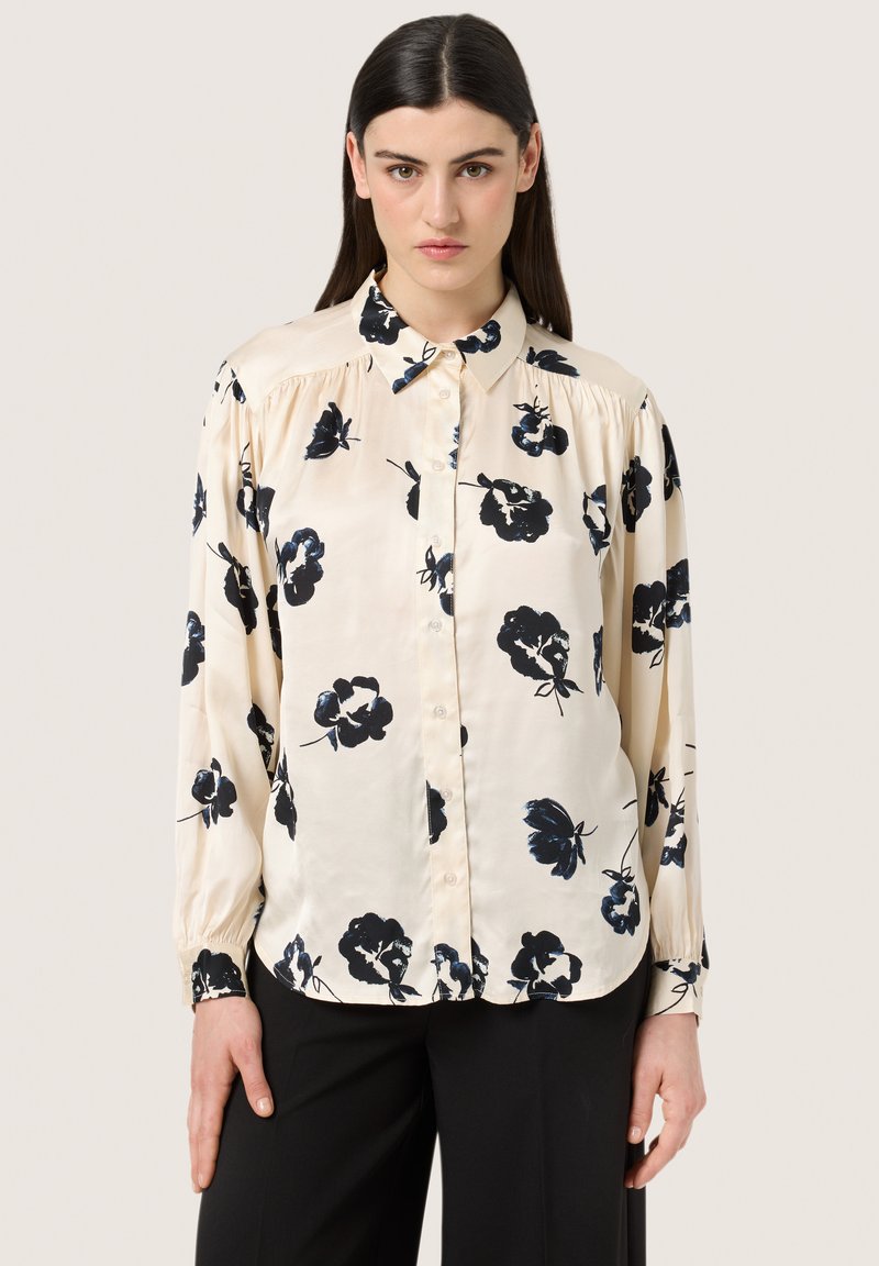 Long-sleeve button-up shirt in cream satin with black floral pattern, featuring a classic collar and elasticized cuffs.