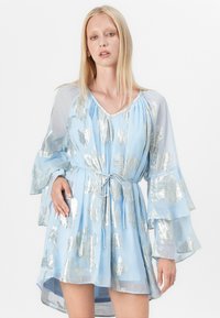 Vestido azul claro com padrão de folhas prateadas cintilantes, mangas largas e fluídas, e cintura com cordão. Tecido semi-transparente com barra em camadas.